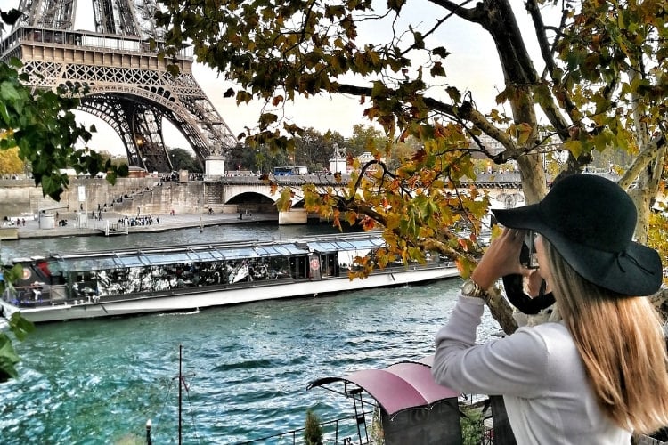 woman taking photo of the eiffel tower sitting near the seine river